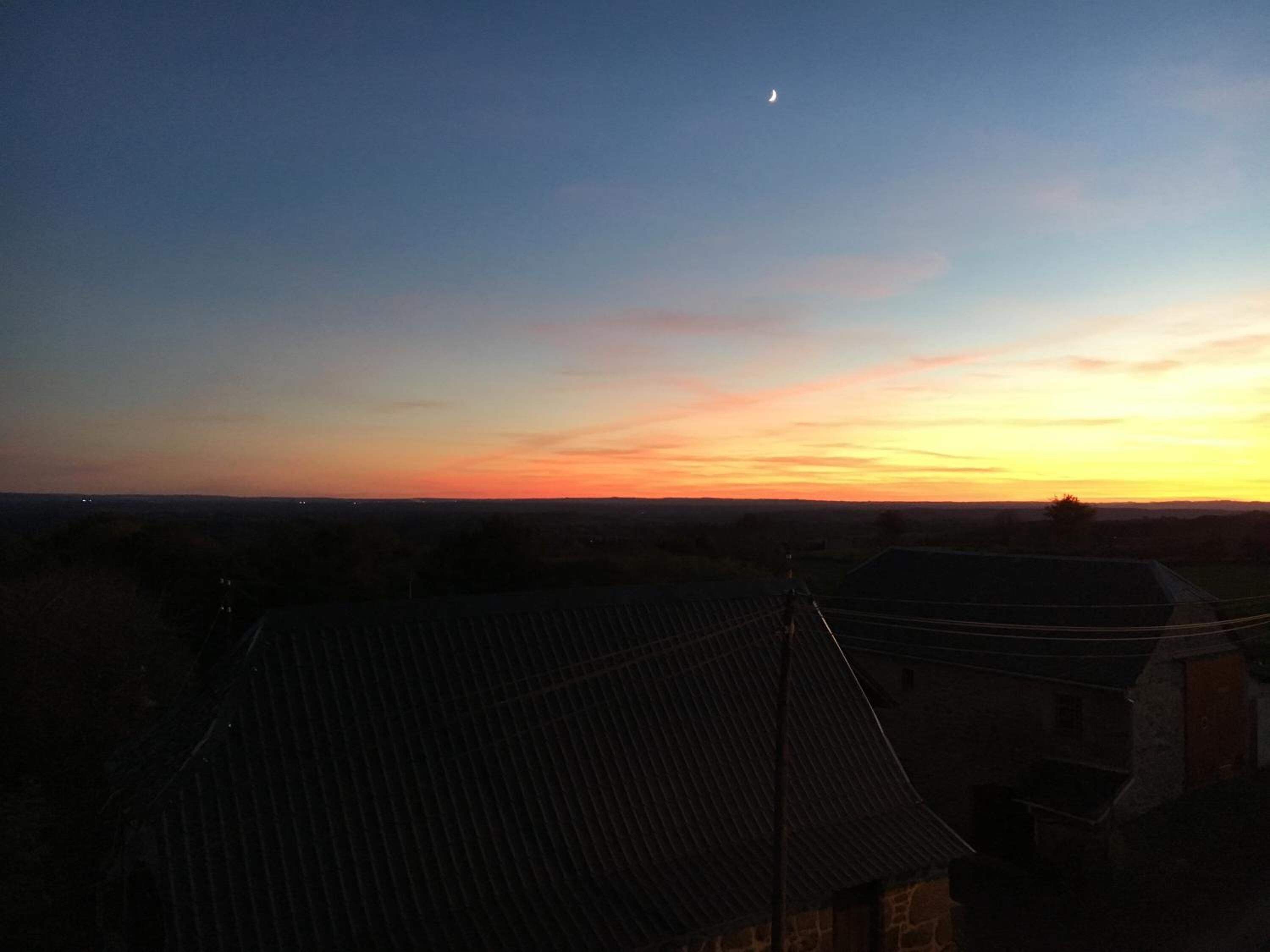 Vista del atardecer desde una zona residencial con tejados de cerámica y un edificio de piedra en primer plano.