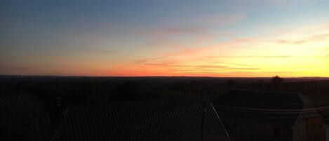 Vista del atardecer desde una zona residencial con tejados de cerámica y un edificio de piedra en primer plano.