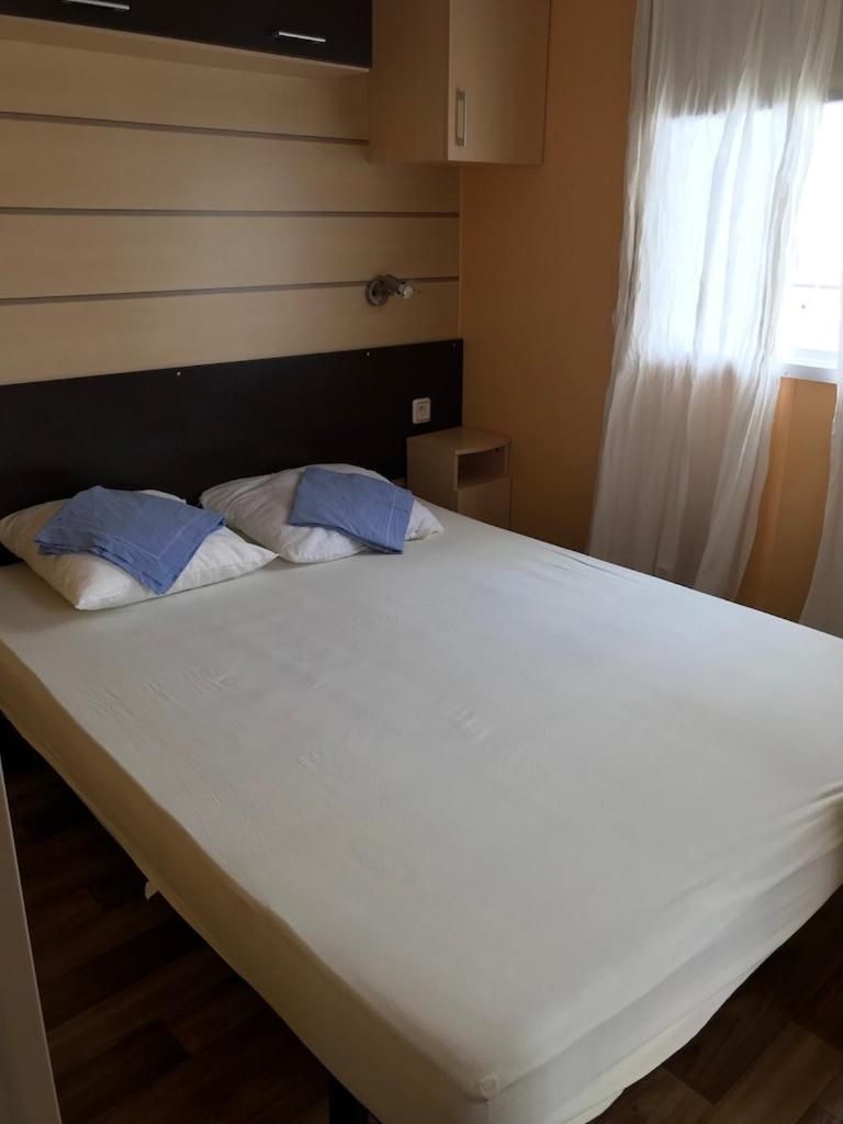 A single bed with a headboard, a bedside table, and a window with curtains.