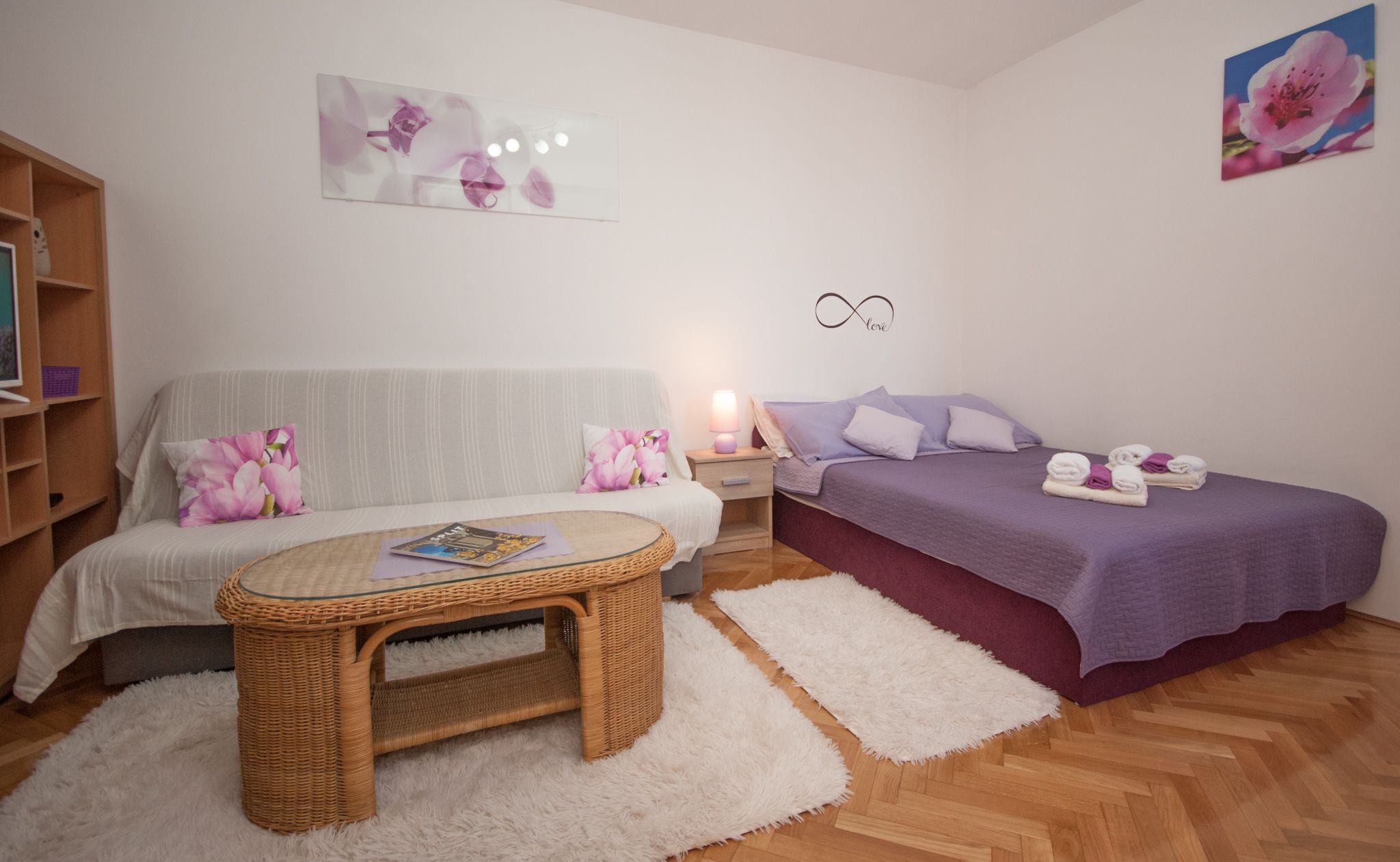 A cozy bedroom with a sofa, a bed, a small round table, and a nightstand with a lamp.