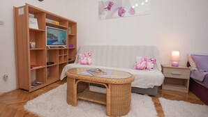 Ein gemütliches Wohnzimmer mit Sofa, Glastisch, Bücherregal und einem an der Wand befestigten Fernseher.