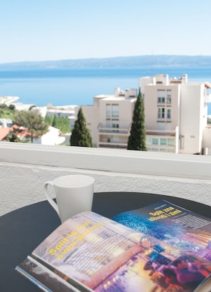 Una mesa con una taza blanca y una revista, con vistas a la costa, edificios y árboles.
