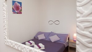 Ein Schlafzimmer mit einem Bett, Kissen, einem Nachttisch, einer Lampe und einem Spiegel mit floralem Dekor.