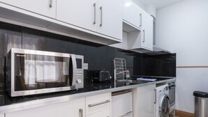 A modern kitchen with white cabinets, a stainless steel microwave, a washing machine, and a black countertop. - Arlo Apartments (Eastbourne)