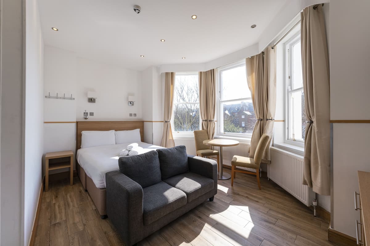A hotel room with a bed, a sofa, a small table, a chair, and a window with curtains.