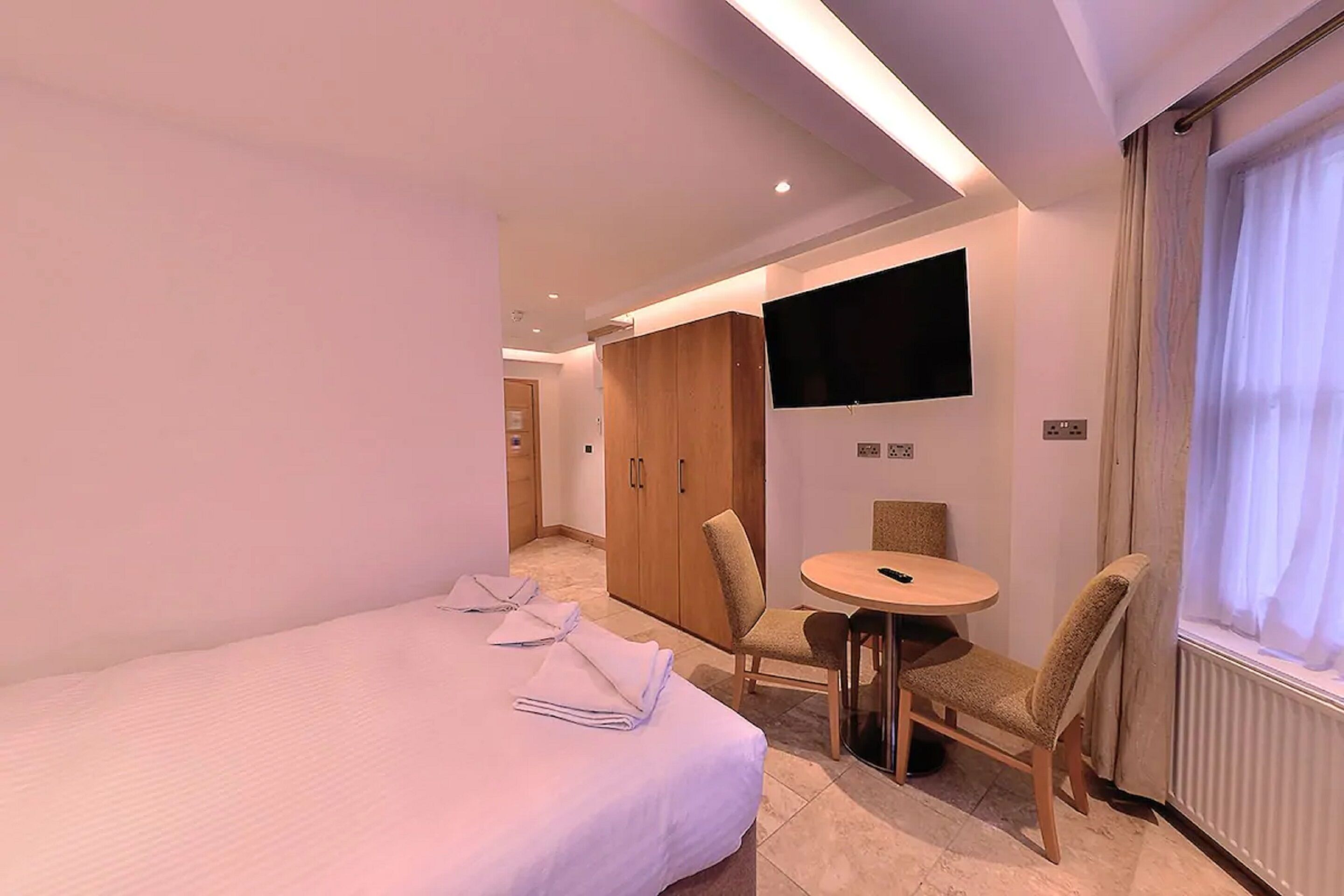 A hotel room with a bed, a TV mounted on the wall, a small round table, and a chair.