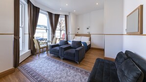 A modern hotel room with a bed, two sofas, a dining table, and a view of the outside. - Arlo Apartments (Eastbourne)