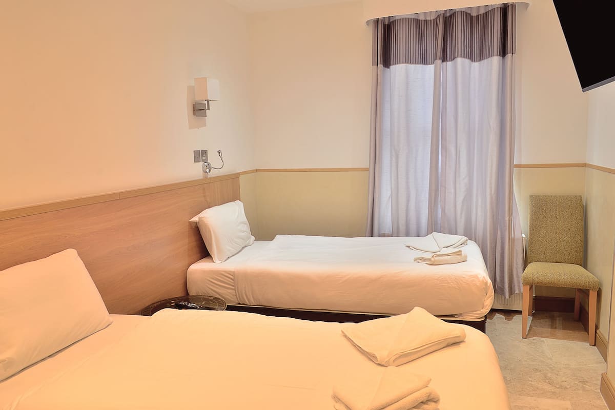 A hotel room with two beds, a chair, a TV, and a window with curtains.