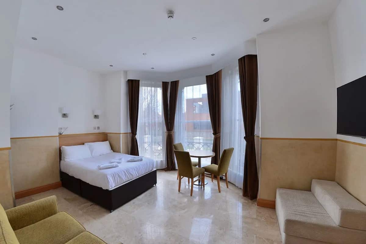 A hotel room with a bed, two chairs, a small table, a TV, and a window with curtains.