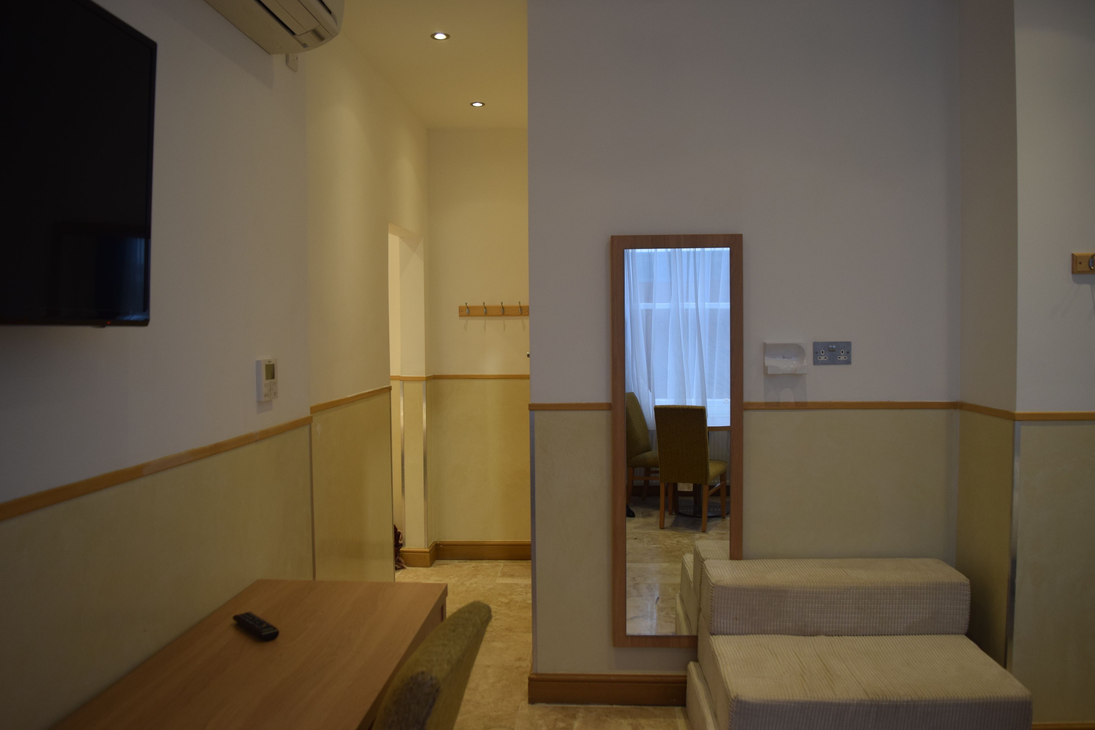 Une chambre d’hôtel avec un bureau en bois, un lit simple et un téléviseur fixé au mur.