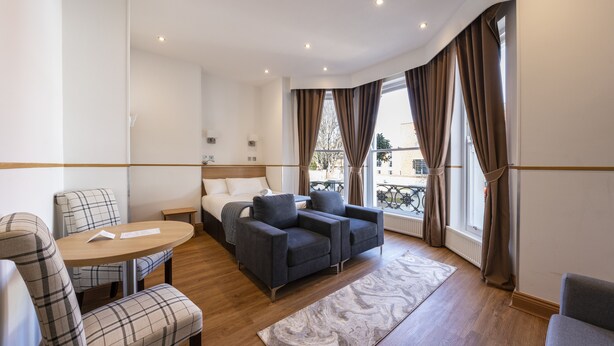 A modern hotel room with a sofa, armchair, and a small table. - Arlo Apartments (Eastbourne)