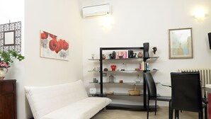 A living room with a white sofa, a black chair, a glass shelf with decorative items, and a framed picture on the wall. - La Terrazza Foscolo - con Parcheggio (Florence)