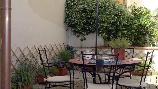 An outdoor patio with a round table and four chairs, a red umbrella, and potted plants. - La Terrazza Foscolo - con Parcheggio (Florence)