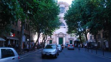 Une rue bordée d’arbres et de voitures garées, qui mène à un bâtiment doté d’une grande entrée et surmonté d’une statue.