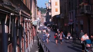 Uma rua urbana movimentada, flanqueada por edifícios históricos, um passeio para pedestres e diversas lojas.