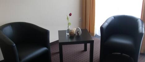 Una habitación con dos sillones de cuero negro, una mesita con un jarrón de una sola rosa roja y una ventana con cortinas.