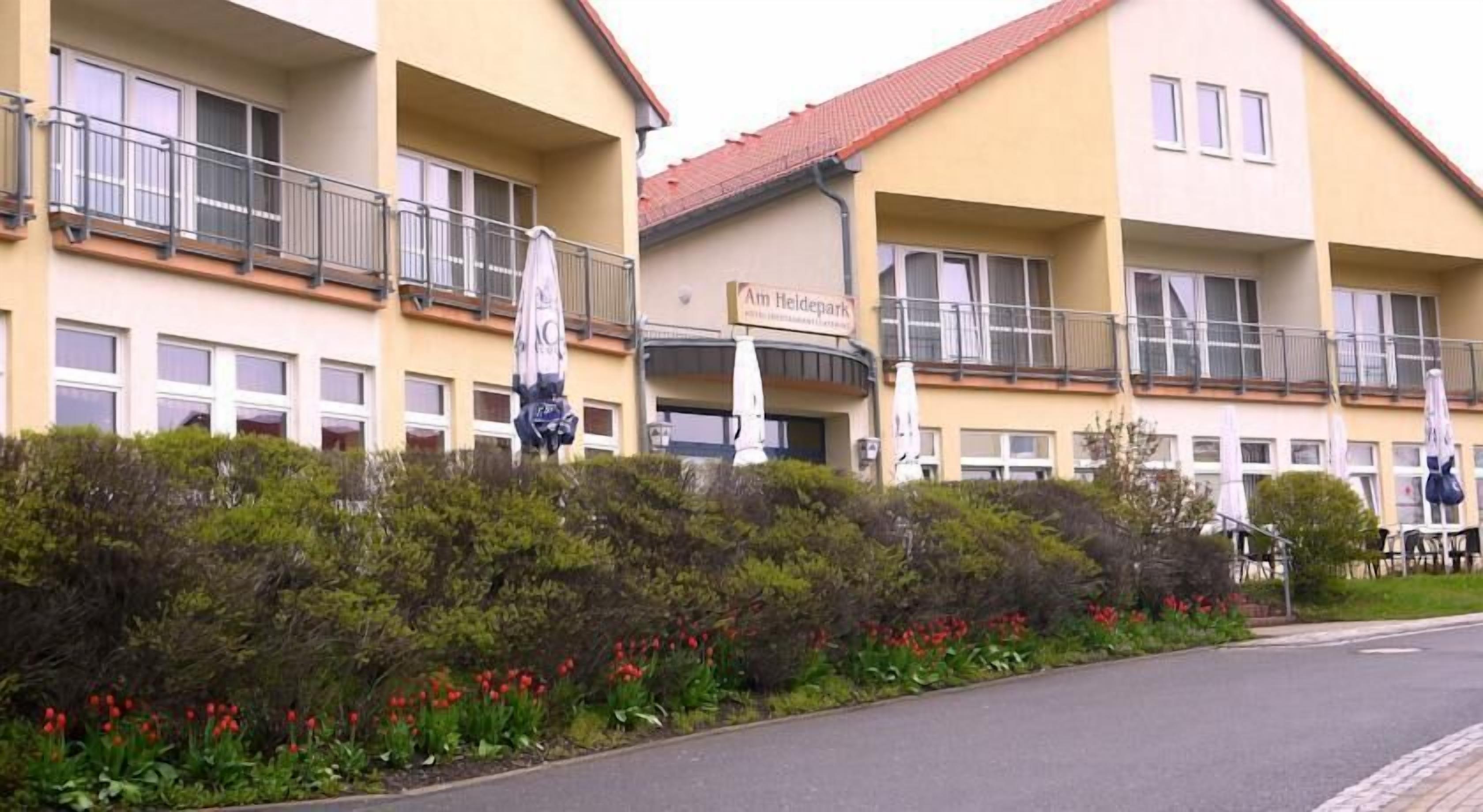A multi-story hotel with balconies, a sign reading "Kim Heidpark," and a landscaped garden with red flowers.