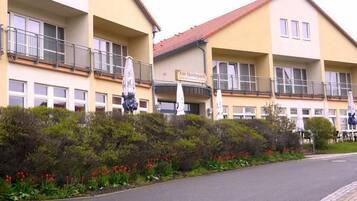 A multi-story hotel with balconies, a sign reading "Kim Heidpark," and a landscaped garden with red flowers.