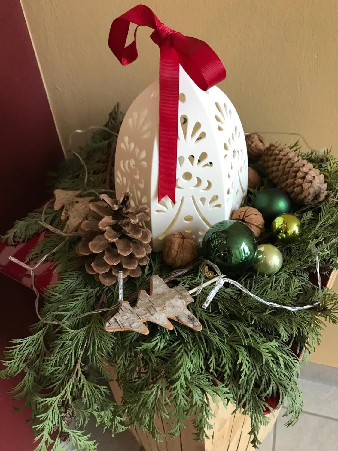 Eine Weihnachtsdekoration mit einem weißen Ei, rotem Band, Zapfen und grünen Ornamenten.