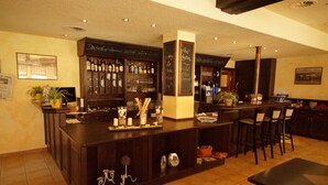 Una zona de bar con un mostrador de madera oscura, estantes con botellas y un menú en una pizarra.