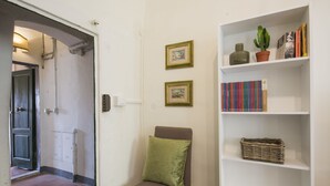 A room with a brown chair, a white shelf with books and a cactus, and a door leading to another room. - Porcellana (Florence)