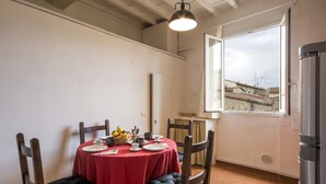 A dining area with a red tablecloth, wooden chairs, and a window with a view of buildings. - Porcellana (Florence)
