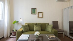 A living room with a green sofa, a coffee table with books and a vase of flowers, a potted plant, and an air conditioning unit. - Porcellana (Florence)