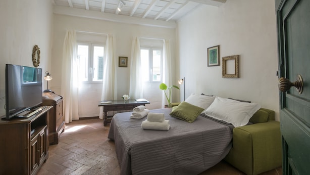 A bedroom with a bed, a television, a desk, and a green door. - Porcellana (Florence)