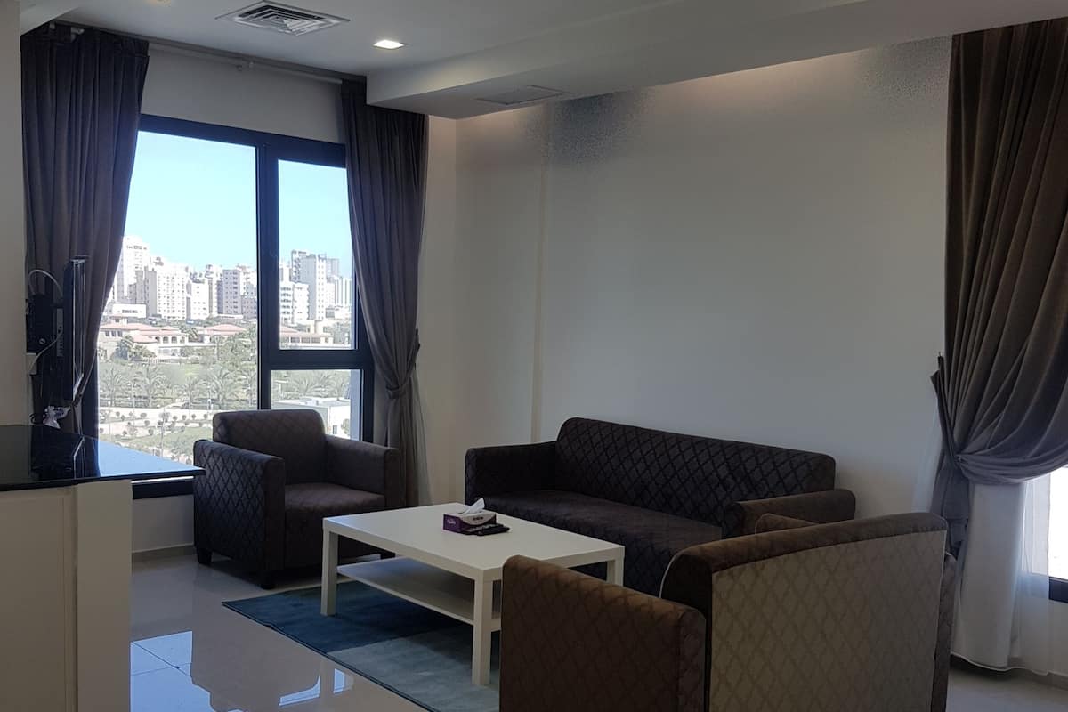 Una sala de estar moderna con un sofá, una mesa de centro y vistas de la ciudad a través de amplios ventanales.