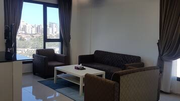 A modern living room with a sofa, coffee table, and a view of the cityscape through large windows.
