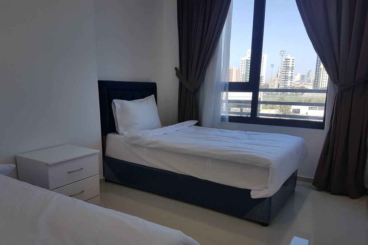 Habitación de hotel moderna con una cama grande, una mesita de noche y vistas a la silueta urbana a través de la ventana.
