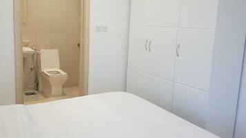 A bedroom with a bed, a wardrobe, and a bathroom with a toilet and sink.