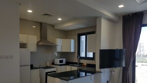 A modern kitchen with white cabinets, a black countertop, a microwave, a stove, and a window with curtains. - Magic Suite Boulevard Salmiya (Salmiya)