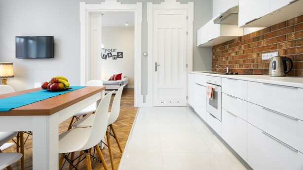 A modern kitchen with white cabinetry, a brick backsplash, and a dining area with a table and chairs.