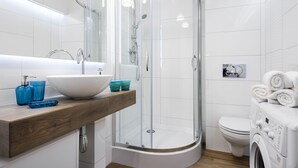 A modern bathroom with a glass-enclosed shower, a white sink, and a built-in washing machine.