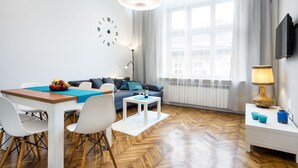 A modern living room with a dining area, a sofa, a coffee table, and a TV mounted on the wall.