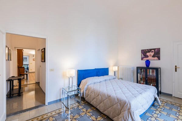 A bedroom with a bed, bedside tables, a radiator, a door, and a hallway leading to a dining area. - Via Guelfa - Ampio Appartamento (Florence)