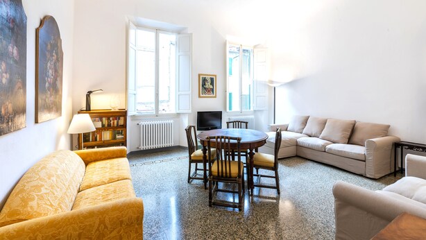 Ein Wohnzimmer mit einer Couch, einem runden Tisch mit Stühlen, einem Fernseher und einem Bücherregal.