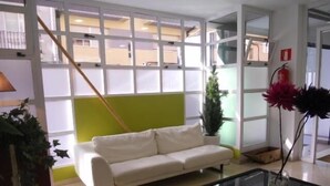 Een kamer met een witte bank, een glazen tafel, een plant in pot en een brandblusser.