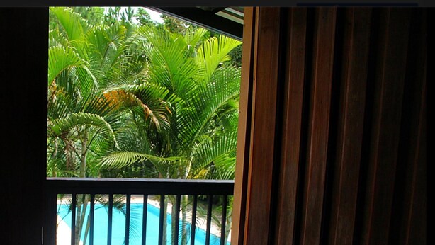 A wooden deck with a view of a blue pool and palm trees. - Hotel Gil Town (Poptun)