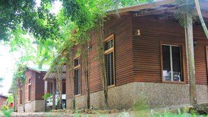 A wooden cabin with a stone foundation, surrounded by lush greenery and a palm tree. - Hotel Gil Town (Poptun)