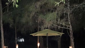 An outdoor dining setup with a table and chairs under a canopy, surrounded by trees. - Hotel Gil Town (Poptun)