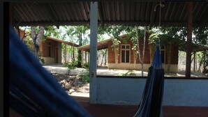 A covered outdoor area with a hammock, wooden buildings, and trees. - Hotel Gil Town (Poptun)