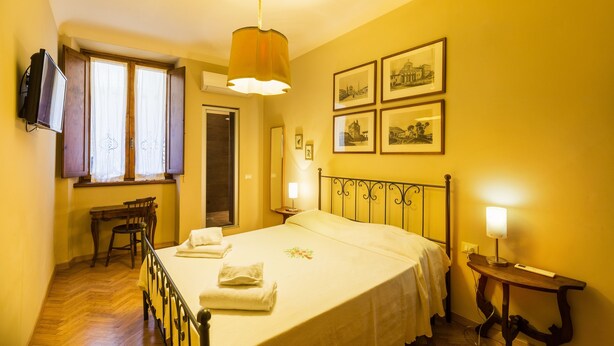 A bedroom with a bed, a desk, and a chair. There are framed pictures on the wall. - Piccolo Sogno (Florence)