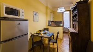 A compact kitchen with a microwave, refrigerator, and wooden cabinet. A dining table with chairs and a small window is visible. - Piccolo Sogno (Florence)