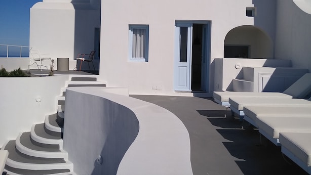 A modern white building with a curved staircase leading to a covered outdoor area with lounge chairs. - Sol Mate Suites (Santorini)