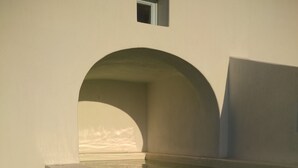 A room with a large arched window, a small window, and a built-in bathtub. - Sol Mate Suites (Santorini)