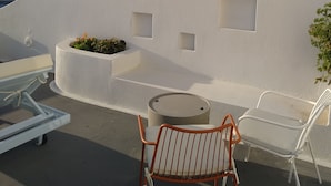 A rooftop terrace with a white wall, a round table, two chairs, and a small planter with flowers. - Sol Mate Suites (Santorini)