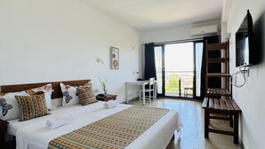A hotel room with a large bed, a desk, a chair, a TV mounted on the wall, and a balcony with a view. - Hotel Ambatoloaka (Nosy Be)