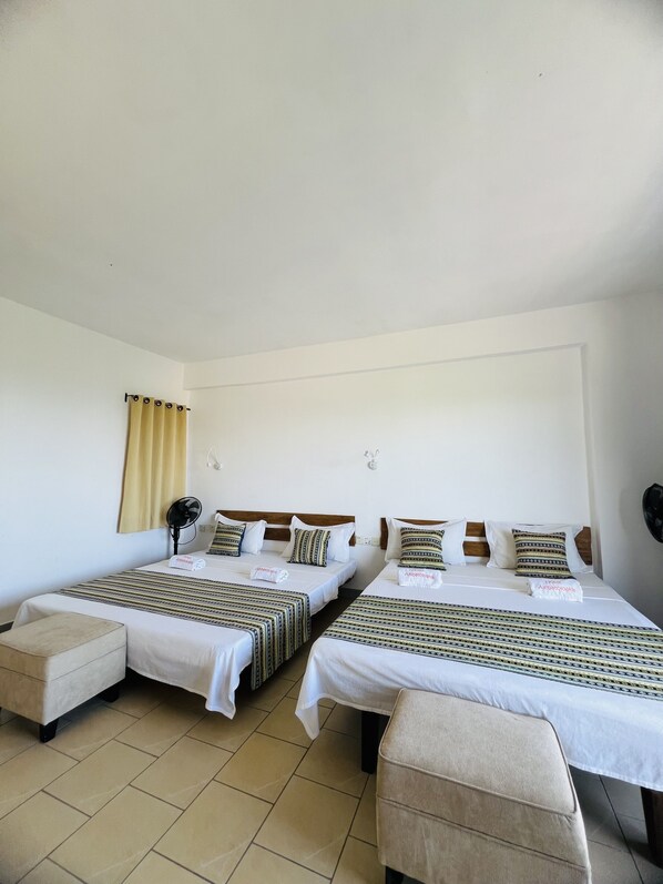 A hotel room with two beds, each with patterned bedding, a bedside table, a chair, and a curtain.